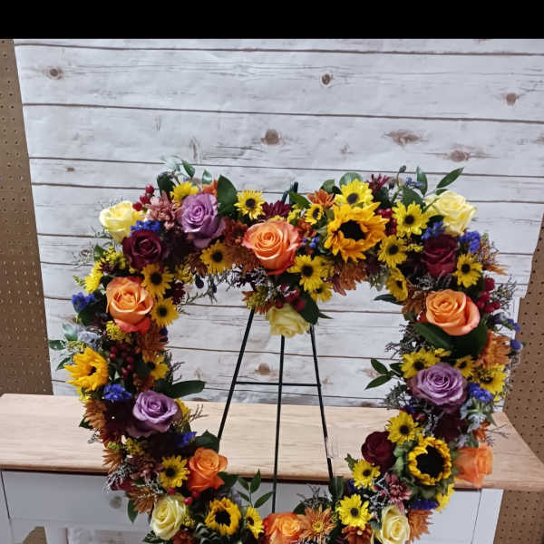Heart-shaped floral wreath on a metal stand with roses and sunflowers