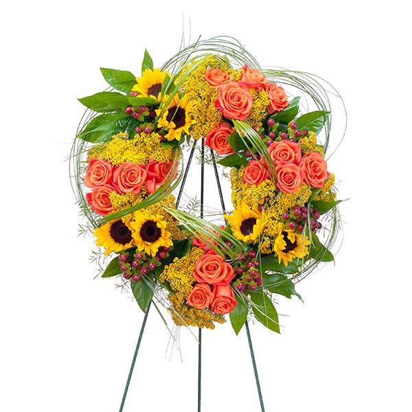 Standing wreath of orange roses and yellow sunflowers with decorative looping grasses