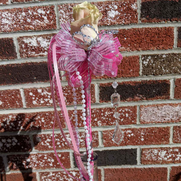 Single pale rose in a tall pink-accented glass bud vase with tiara, bow, pearls, and crystals.