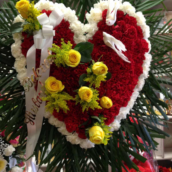 Heart-shaped red and white floral wreath with yellow roses and ribbon