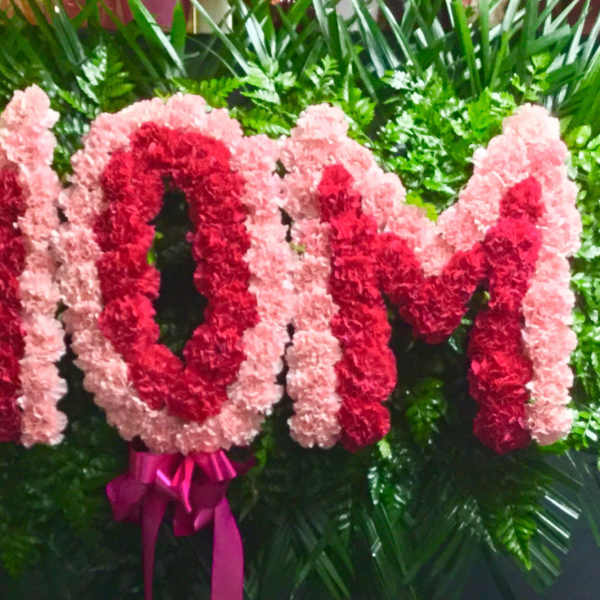Pink and red floral arrangement spelling MOM with a ribbon bow