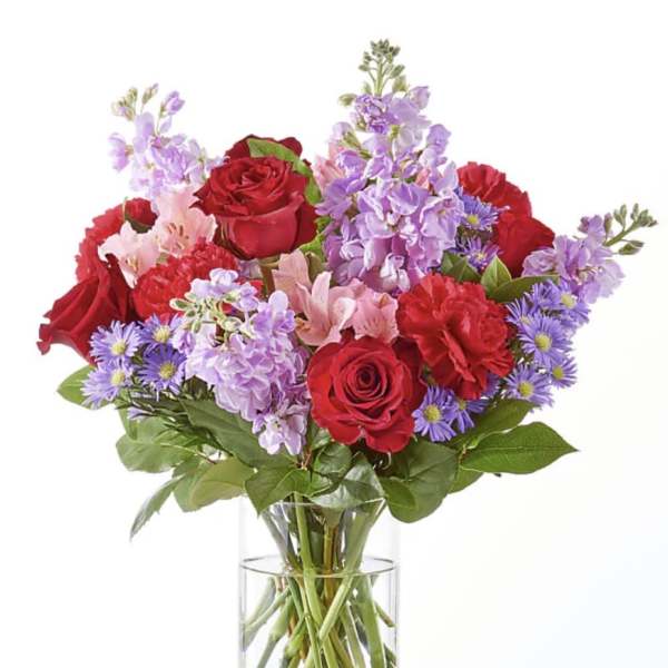 Bouquet of red roses and purple flowers in a clear glass vase