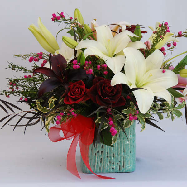 Bouquet of white lilies and red roses in a turquoise vase with a red ribbon