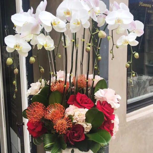 Tall floral arrangement with white orchids and red roses in a white vase