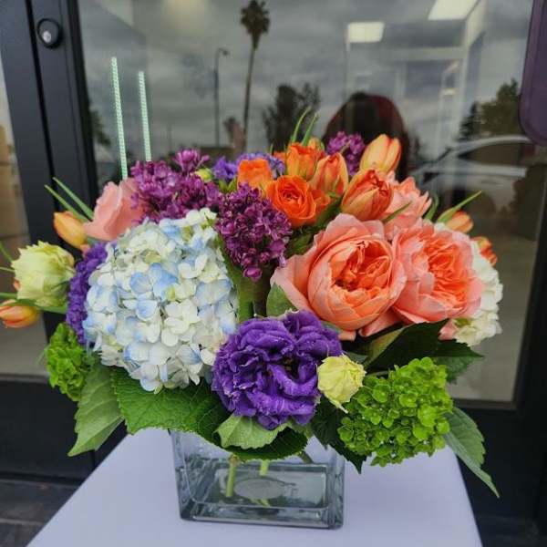 Low arrangement of bright mixed flowers in a clear glass cube vase