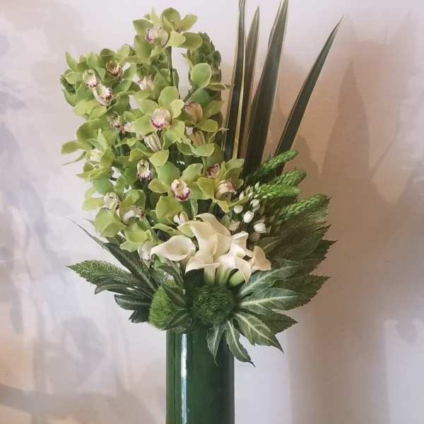 Tall green floral arrangement with orchids and calla lilies in a glass vase