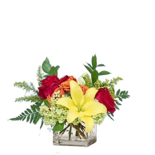Bouquet of red roses, yellow lilies, and orange flowers in a clear square vase