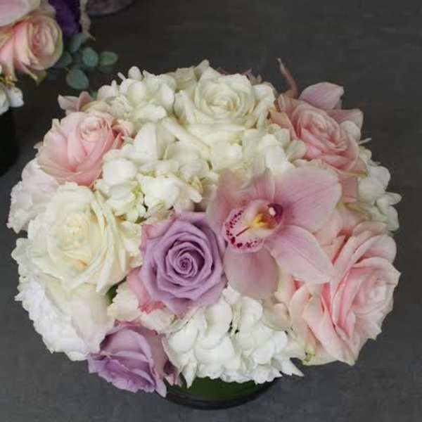 Round bouquet of pink, white, and lavender flowers in a low container