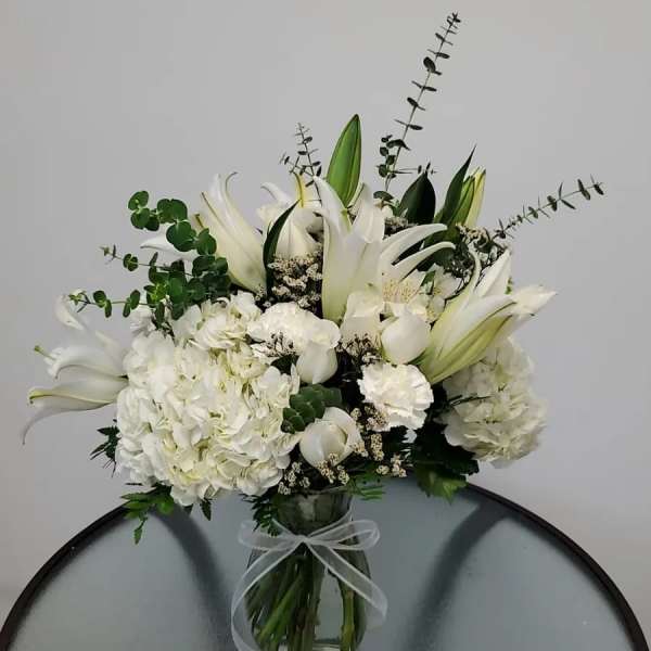 White lilies and hydrangeas arranged in a glass vase with a ribbon.