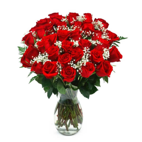 Tall bouquet of red roses with white filler flowers arranged in a clear glass vase