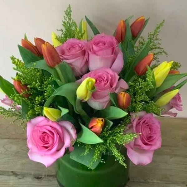 Pink roses and orange-yellow tulips in a green glass vase