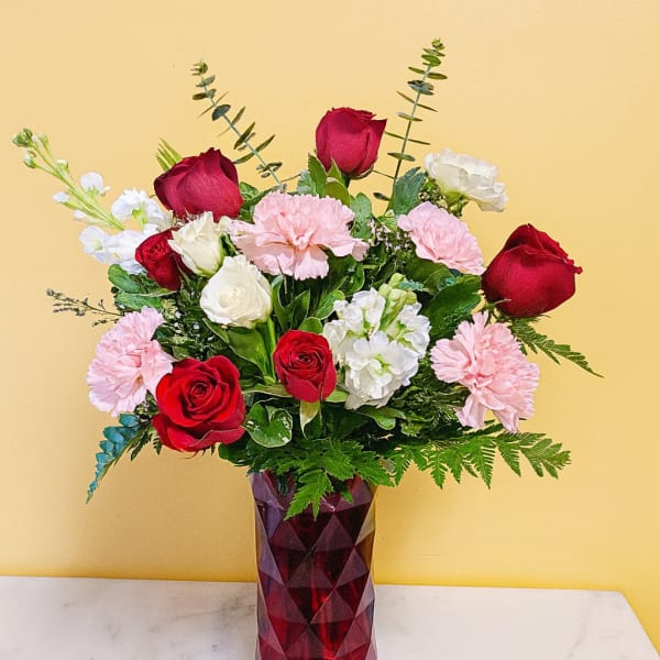 Red roses, pink carnations, and white blooms in a faceted red glass vase