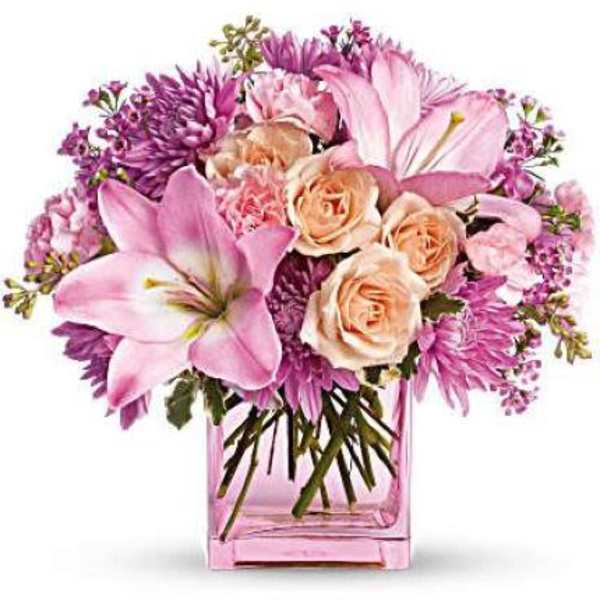 Pink and peach lilies, roses, and mums arranged in a pink glass cube vase