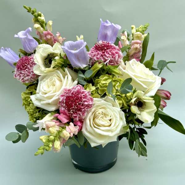 Mixed bouquet of white roses, pink carnations, and lavender blooms in a dark vase