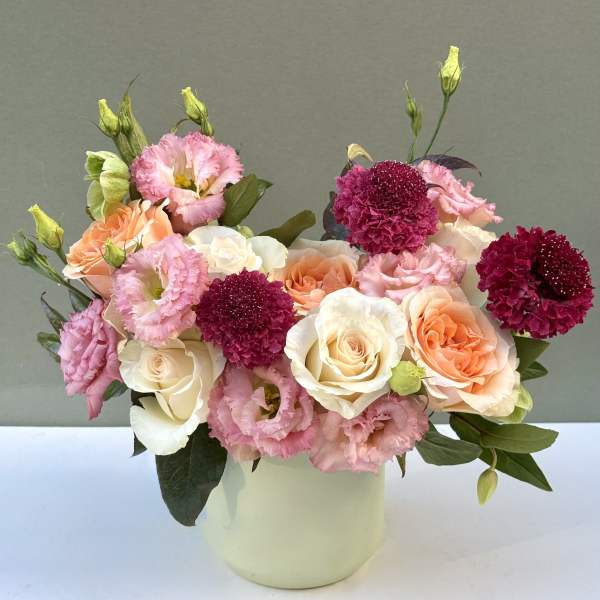 Pink and peach roses with magenta blooms in a white vase