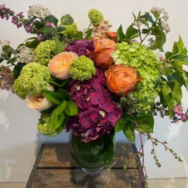 Mixed bouquet of orange roses, green hydrangeas, and purple blooms in a glass vase