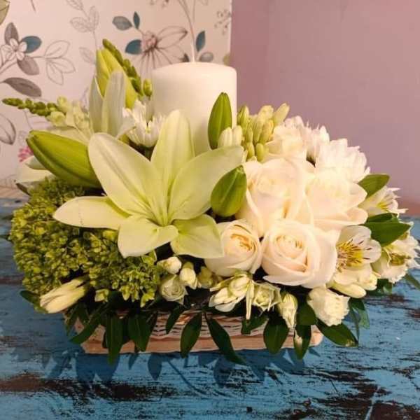 White lilies and roses arranged in a low basket with a candle