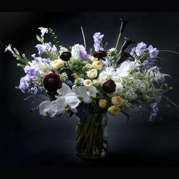 Mixed bouquet of white, lavender, and dark red flowers in a glass vase