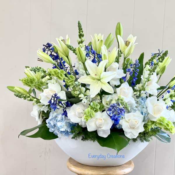 White lilies and roses arranged in a white bowl with blue accents