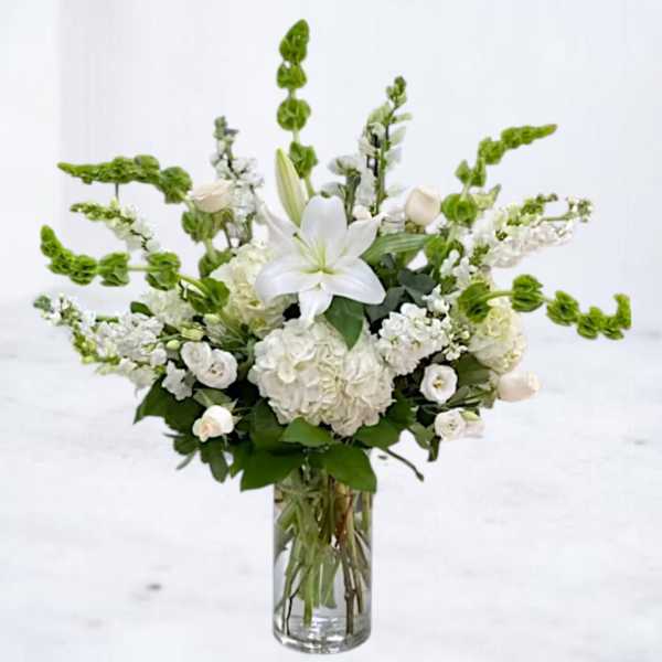 White lilies and hydrangeas in a clear glass vase with green snapdragons