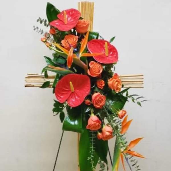 Tall bamboo cross spray with orange roses, red anthuriums, and birds of paradise on a stand