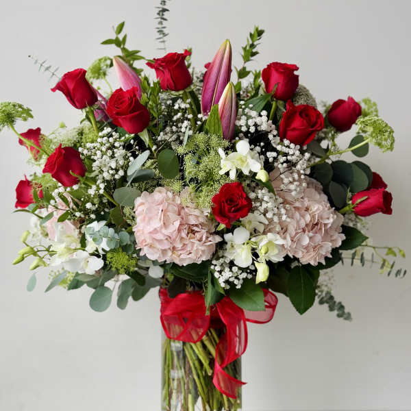 Red roses and pink lilies in a clear glass vase with a red ribbon