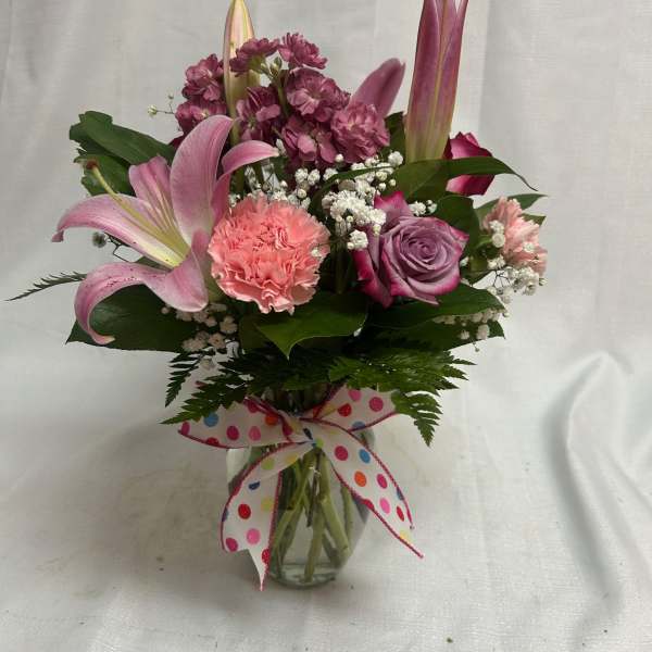 Mixed pink and purple flower arrangement in a clear vase with a polka dot bow