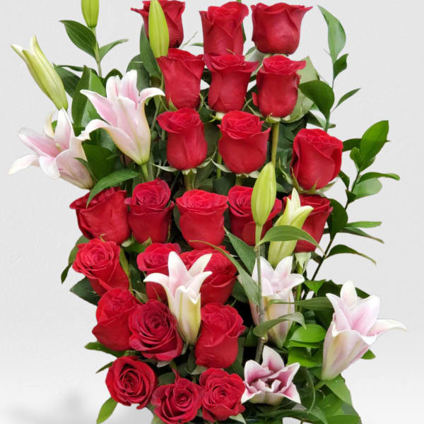 Tall arrangement of red roses and white lilies in a square glass vase
