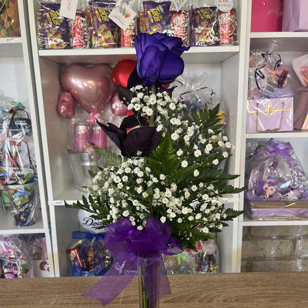Tall purple rose and white filler flowers in a clear glass vase with a purple bow