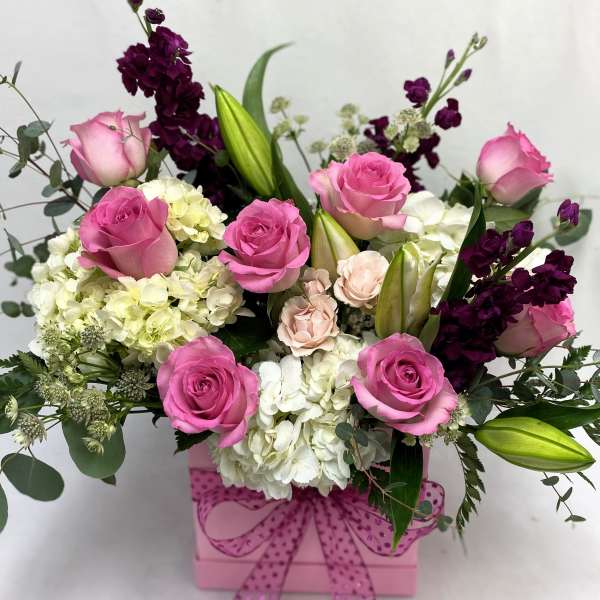 Pink and white flower arrangement in a pink box with a bow