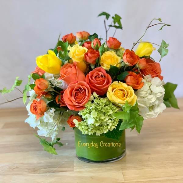 Orange and yellow roses with white hydrangeas in a glass vase