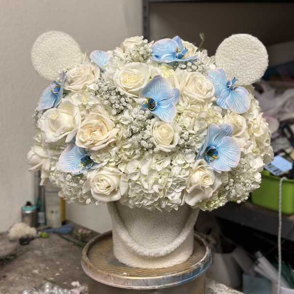 White floral arrangement with blue orchid accents on a textured stand