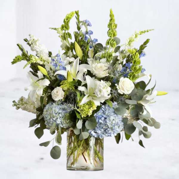 White lilies and roses with blue hydrangeas in a glass vase