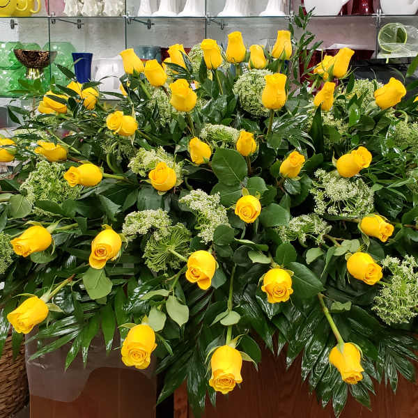 Large horizontal spray of yellow roses with green filler flowers arranged on a wooden base
