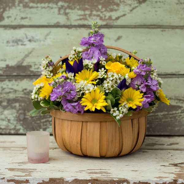 Basket of yellow and purple flowers with a small frosted glass candle