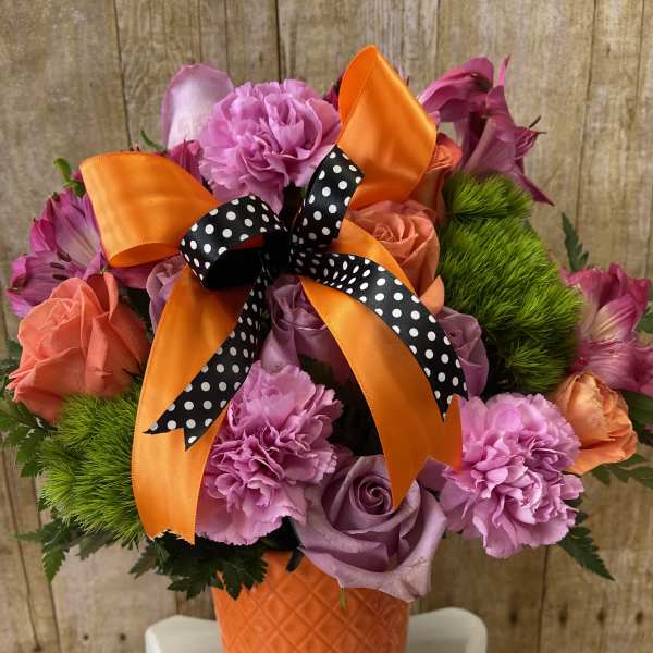 Pink and lavender bouquet in an orange vase with a polka-dot ribbon
