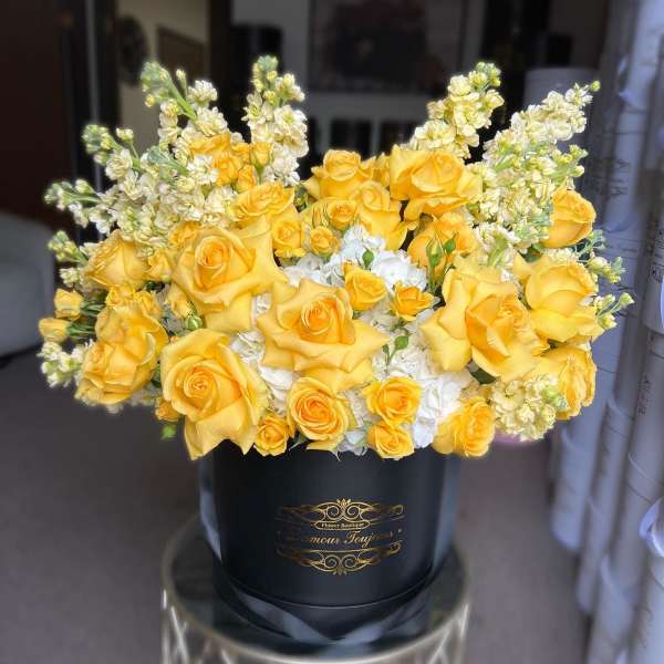 Round black hatbox of yellow roses with white hydrangeas and creamy stock flowers