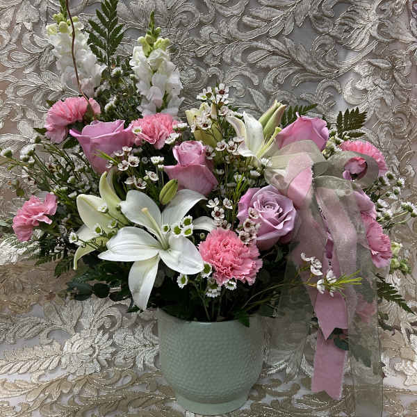 Pink and white floral arrangement in a pale green vase with a ribbon bow