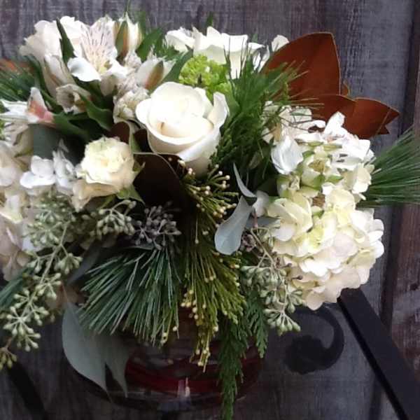 White floral arrangement in a glass vase with pine accents