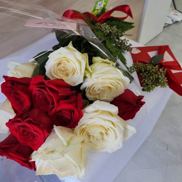 Bouquet of red and white roses with a red ribboned gift box on a white surface