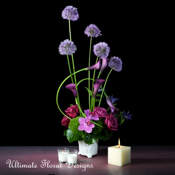 Purple floral arrangement in a white vase with candles nearby