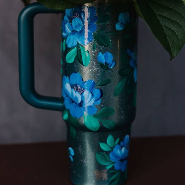 Floral-decorated teal travel mug with blue flowers and green leaves