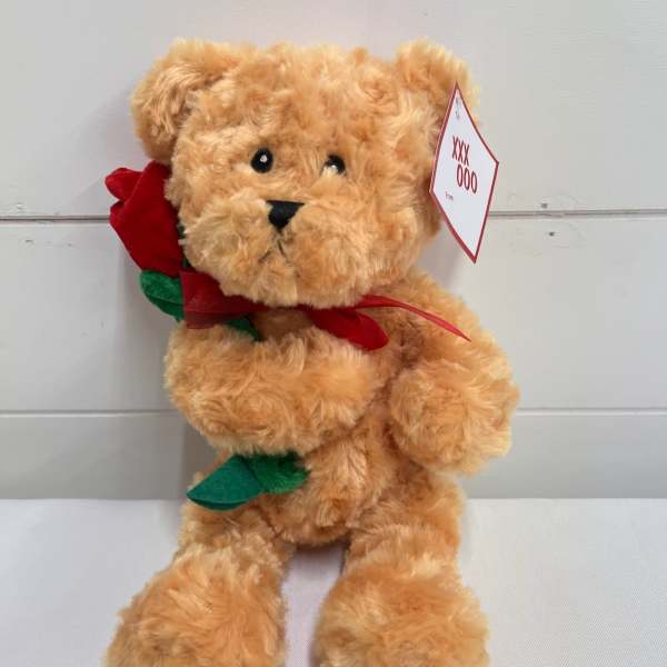Tan teddy bear holding a red fabric rose with a tag on its ear