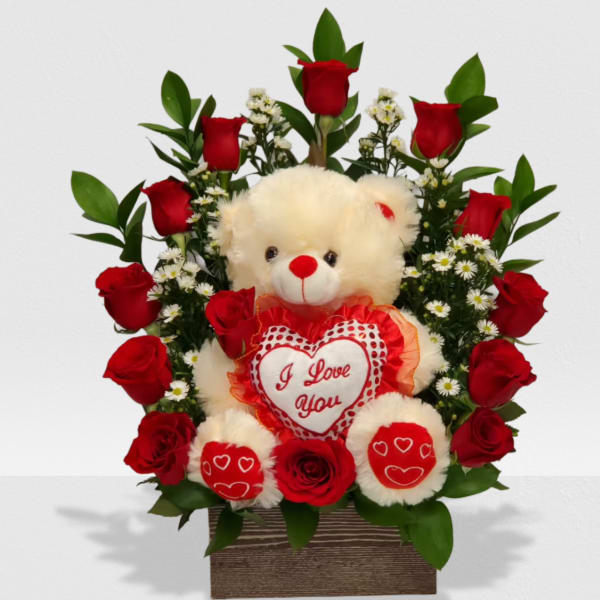Plush bear holding an 'I Love You' heart framed by red roses and white daisies in a wooden box.