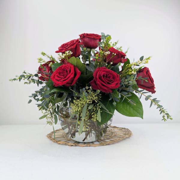 Red roses arranged in a clear glass vase with greenery