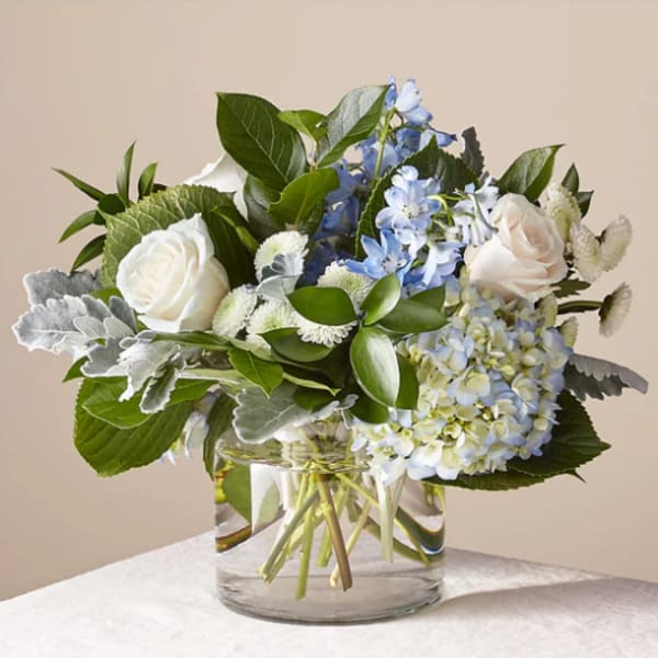 White roses and blue flowers in a clear glass vase