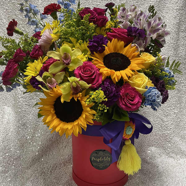 Mixed bouquet with sunflowers, roses, orchids, and alstroemeria in a red hatbox