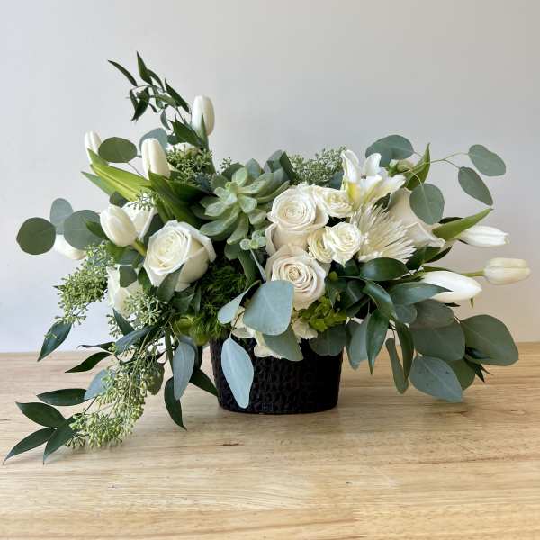White floral arrangement in a black vase with eucalyptus and succulents