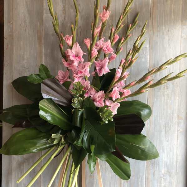 Tall arrangement of pink flowers with large glossy leaves on a wooden stand