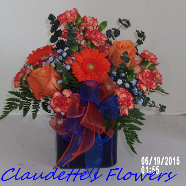 Orange and red flower arrangement in a dark vase with ribbon